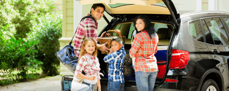 A family packing bags and gear into their car, preparing for a trip, with smiles and a relaxed, happy atmosphere.